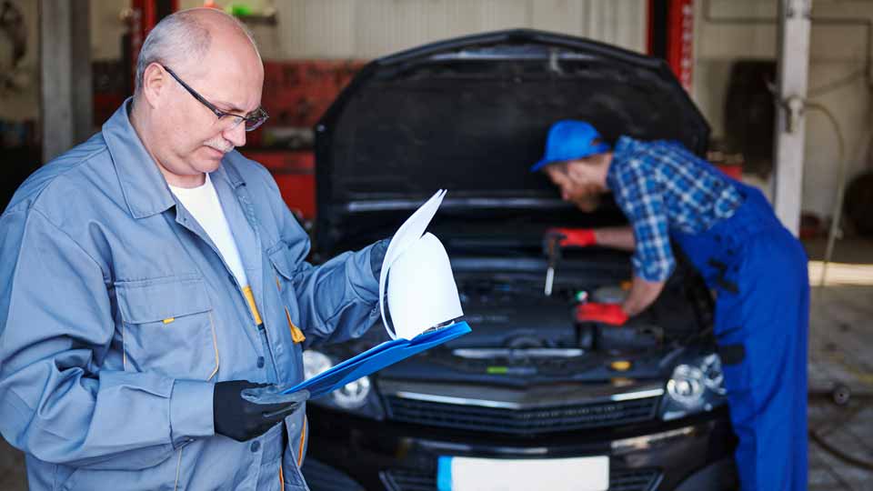 Ein Mechaniker prüft die Unterlagen, während ein anderer den Motor eines Autos kontrolliert