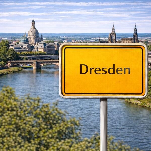 Gelbes Ortsschild Dresden mit Stadt im Hintergrund